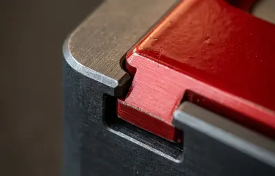 Makroaufnahme einer Schwalbenschwanz-Verbindung aus gefrästem Metall, ein Bauteil in rotem Lack – Symbol für präzise Schnittstellen